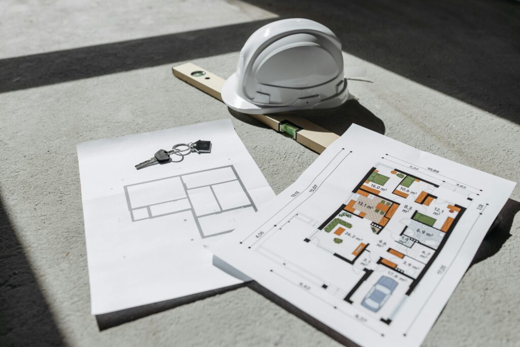 Architectural floor plans with helmet and keys on sunlit floor, perfect for real estate or construction themes.